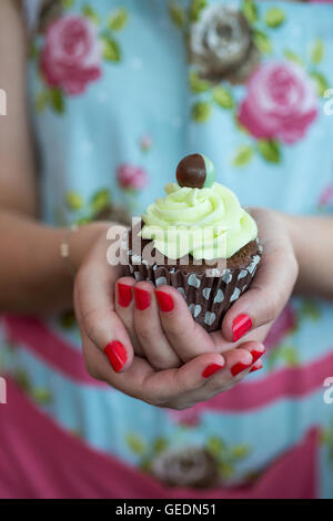 Frauenhand hält einen Schokoladen Cupcake mit Minze Zuckerguss gekrönt Stockfoto