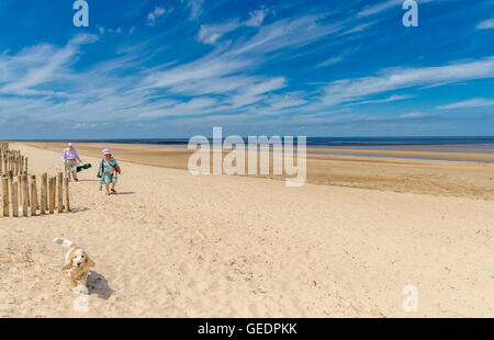 Älteres Ehepaar zu Fuß auf den Sand mit ihrem Hund bei Holme nächsten Sea, Norfolk, England. Stockfoto