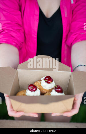 Frau in rosa Strickjacke Oberseite hält drei Mandel Cupcakes oder Brötchen mit Mandelscheiben obendrauf, fertig mit Buttercreme Rohrleitungen und Stockfoto