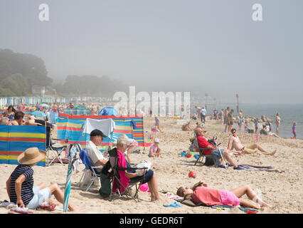 Britische Sommer Urlauber genießen die warmen Temperaturen am Strand von Avon in Dorset, obwohl Meer Nebel die Sonne, UK verdeckt Stockfoto