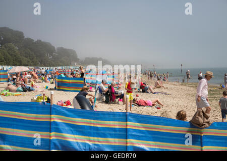 Britische Sommer Urlauber genießen die warmen Temperaturen am Strand von Avon in Dorset, obwohl Meer Nebel die Sonne, UK verdeckt Stockfoto