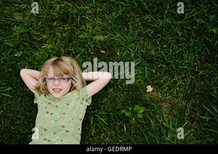 Junges Mädchen mit Brille, die Verlegung auf dem Rasen, High Angle View Stockfoto