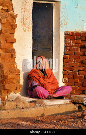 Unbekannte indische Frau in orange Sari sitzt auf einer Veranda des Hauses. Stockfoto