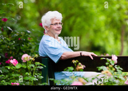 Glücklich senior Behinderte Dame mit einer Gehbehinderung, genießen Sie einen Spaziergang in einem sonnigen Park schieben ihre Gehhilfe oder Rollstuhl Stockfoto