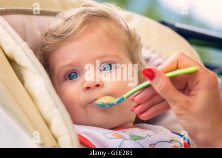 Eine Mutter füttert ihr Baby Boy mit Löffel im Freien. Stockfoto