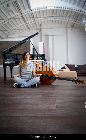 Jungen Doppel Bass-Spieler sitzen auf dem Boden vor einem Flügel. Stockfoto