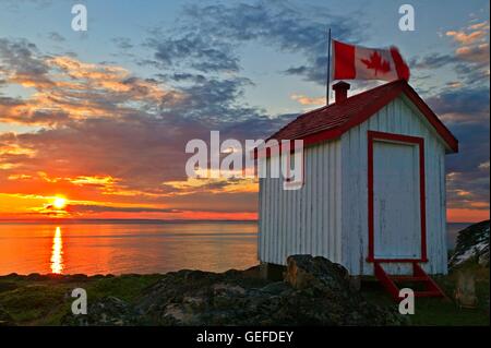 Geographie / Reisen, Kanada, Neufundland, einer echten kanadischen Plumpsklo bei Sonnenuntergang mit einer kanadischen Flagge auf Quirpon Insel vor der Great Northern-Halbinsel in Neufundland, mit Blick auf die malerische Strait Of Belle Isle Stockfoto