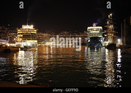 Zwei Kreuzfahrtschiffe und die Sail training ship Tenacious im Hafen von Funchal, Madeira, mit den Lichtern von Funchal hinter. Stockfoto