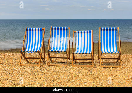 Reihe von vier leere Liegestühle auf einem Kiesstrand an der sonnigen Küste in Kent, UK Stockfoto