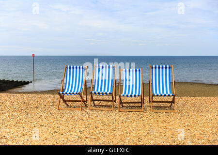 Reihe von vier leere Liegestühle auf einem Kiesstrand an der sonnigen Küste in Kent, UK Stockfoto