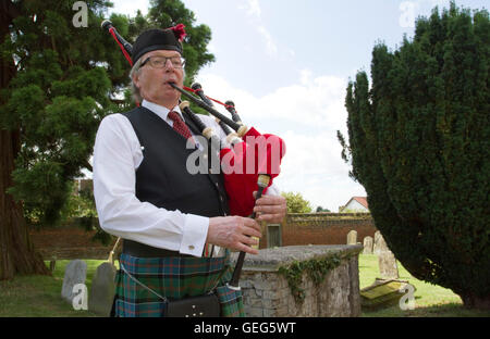 Eine schottische Piper in traditioneller Kleidung in einem englischen Kirchhof für eine Hochzeit Stockfoto