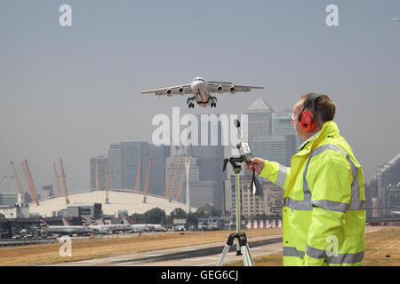Ein Umwelt-Ingenieur überwacht Lärmpegel am London City Airport Flugzeug startet. Canary Wharf im Hintergrund. Stockfoto