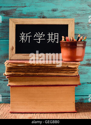 eine Tafel mit dem Text zurück zur Schule geschrieben in Japanisch und in einen Topf mit einigen Bleistiften auf einem Stapel alter Bücher, platziert auf einem ru Stockfoto