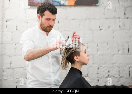 Friseur schneidet Haare mit einer Schere auf Krone schöner zufriedener Kunde in professionellen Coiffeur-salon Stockfoto