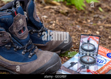 Paar Wanderstiefel mit Karte und Kompass, auf einem Waldboden. Stockfoto