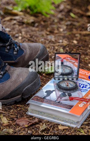 Paar Wanderstiefel mit Karte und Kompass, auf einem Waldboden. Stockfoto