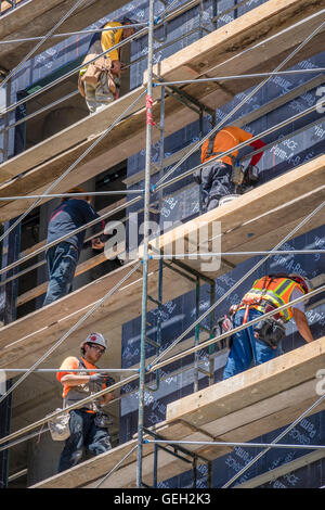 Fünf Bau-Arbeiter arbeiten auf verschiedenen Ebenen von Gerüsten während der Entwicklung des Hochhauses Stockfoto