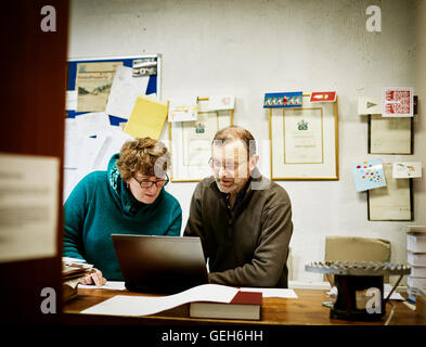Zwei Menschen sitzen an einem Computer in einer kleinen Buchbinderei-Geschäft. Stockfoto
