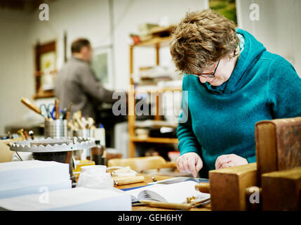 Eine Frau arbeitet an einem digital-Tablette, umgeben von Buch Bindung Werkzeuge und Geräte. Stockfoto