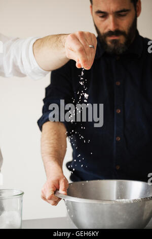 Zwei Bäcker an einem Tisch stehend, Brotbacken, Prise Salz in eine Rührschüssel Metall. Stockfoto