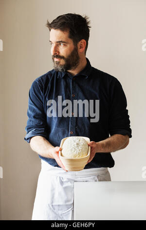 Baker, die holding eines frisch gebackenen Laib Weißbrot in ein proofing Korb Rattan. Stockfoto