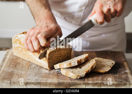 Nahaufnahme eines Bäckers ein frisch gebackenes Brot mit einem Brotmesser aufschneiden. Stockfoto
