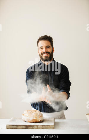 Baker, wischte seinen mehligen Händen, ein frisch gebackenes Brot auf ein Schneidebrett. Stockfoto