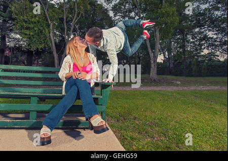 Mann küsst seine Freundin beim springen hoch in die Luft, stützte sich auf eine Bank Stockfoto