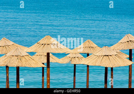 Stroh Sonnenschirme an einem leeren Strand mit türkisfarbenem Wasser im Hintergrund Stockfoto