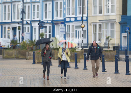 zwei Frauen und ein Mann zu Fuß entlang einer Promenade im Regen Stockfoto