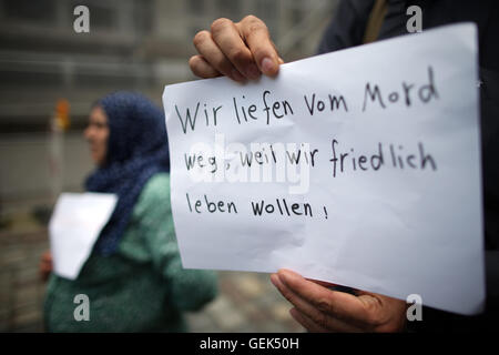 Ansbach, Deutschland. 26. Juli 2016. Flüchtlinge aus Syrien steht nahe dem Aufstellungsort des Angriffs und hält ein Schild geschrieben mit "wir von Mord weggelaufen weil wir friedlich leben wollen" in Ansbach, Deutschland, 26. Juli 2016. in einem mutmaßlichen islamistischen motivierten Angriff auf 24. Juli 2016 wurden 15 Menschen verletzt. Der mutmaßliche Täter, 27-Year-Old Flüchtling aus Syrien, wurde bei der Explosion getötet. Foto: DANIEL KARMANN/Dpa/Alamy Live News Stockfoto