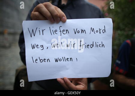 Ansbach, Deutschland. 26. Juli 2016. Flüchtlinge aus Syrien steht nahe dem Aufstellungsort des Angriffs und hält ein Schild geschrieben mit "wir von Mord weggelaufen weil wir friedlich leben wollen" in Ansbach, Deutschland, 26. Juli 2016. in einem mutmaßlichen islamistischen motivierten Angriff auf 24. Juli 2016 wurden 15 Menschen verletzt. Der mutmaßliche Täter, 27-Year-Old Flüchtling aus Syrien, wurde bei der Explosion getötet. Foto: DANIEL KARMANN/Dpa/Alamy Live News Stockfoto
