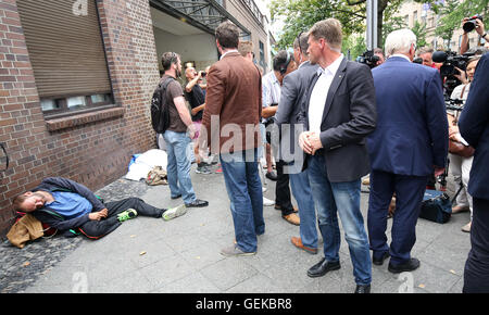 Berlin, Deutschland. 27. Juli 2016. Bodyguards schützen deutsche Innenminister Foreign Affairs Frank-Walter Steinmeier (R), wie er eine Erklärung nach seinem Besuch in der evangelischen Mission im Zoologischer Garten Bahnhof in Berlin, Deutschland, 27. Juli 2016 liefert. Auf der linken Seite schläft ein Obdachloser auf der Straße. Foto: WOLFGANG KUMM/Dpa/Alamy Live News Stockfoto