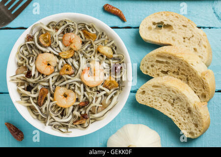 Surimi Glasaale mit Garnelen, Knoblauch, Pfeffer, Brot und Gabel auf einem blauen Holztisch Stockfoto