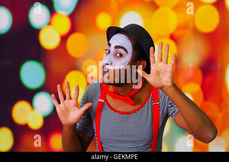 Pantomime-Mann mit Gesichts-Farbe posiert für die Kamera Interaktion lustig mit Händen, verschwommenen Lichtern Hintergrund Stockfoto