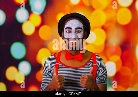 Pantomime-Mann mit Gesichts-Farbe posiert für die Kamera Interaktion gebende Daumen hoch lächelnd, verschwommenen Lichtern Hintergrund Stockfoto