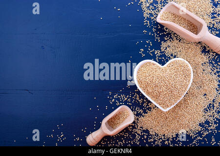 Ich liebe Quinoa-Konzept mit weißer Maserung Quinoa in weiße Herzförmige Schüssel auf einem dunkelblauen Hintergrund Holz. Stockfoto