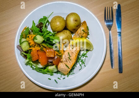 Gebratener Lachs Essen serviert mit gerösteten Babykartoffeln und Tomaten, Gurke und Karotte Salat Stockfoto