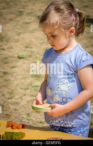 Kleines Mädchen mit dem Holzpuzzle auf dem Spielplatz spielen Stockfoto