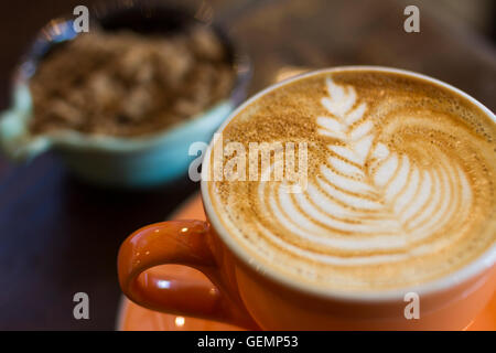 Flache weiße Kaffee in ein orange-Tasse und Untertasse mit blau Zuckerdose im Hintergrund Stockfoto