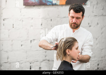 Friseur schneidet Haare mit einer Schere auf Krone schöner zufriedener Kunde in professionellen Coiffeur-salon Stockfoto