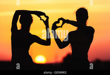 Landschaft mit Silhouette der junge sportliche Frauen Hand in Hand in Herzform auf dem Hintergrund der bunten Himmel bei Sonnenuntergang Stockfoto