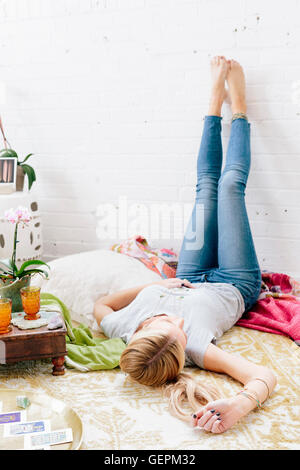 Eine junge Frau in Jeans Lyng auf dem Rücken mit den Beinen gegen die Wand. Stockfoto