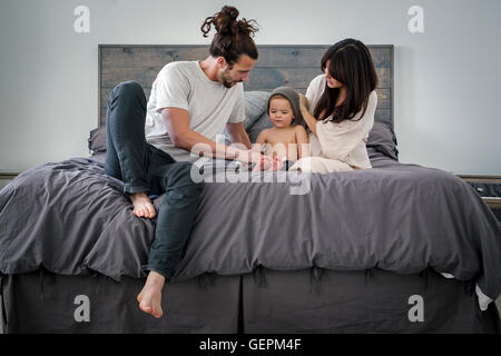 Ein junges Paar und ihr junger Sohn sitzen zusammen auf ihrem Bett. Stockfoto