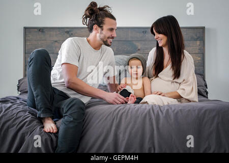 Ein junges Paar und ihr junger Sohn sitzen zusammen auf ihrem Bett. Stockfoto