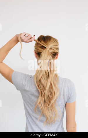 Eine junge Frau mit langen blonden welliges Haar. Einen Pferdeschwanz binden. Hinten Sie Ansicht von. Stockfoto
