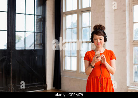 Junge Frau mit Kopfhörern, stehend in einem Proberaum, Musik hören. Stockfoto