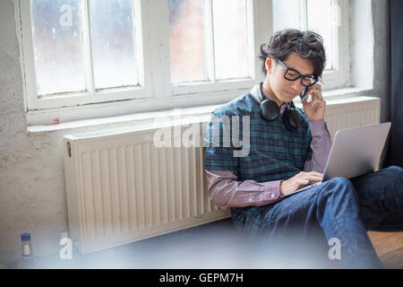 Junger Mann sitzt auf dem Boden in einem Proberaum mit einem Laptopcomputer. Stockfoto