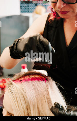 Ein Haar Kolorist Handschuhe rote Haare färben auf einem Client blondes Haar mit einer Bürste anwenden. Stockfoto