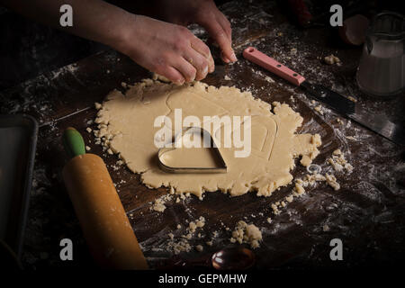 Valentinstag Backen. Frauenbeschneidung Herz geformte Gebäck aus Teig auf einer bemehlten Fläche. Stockfoto